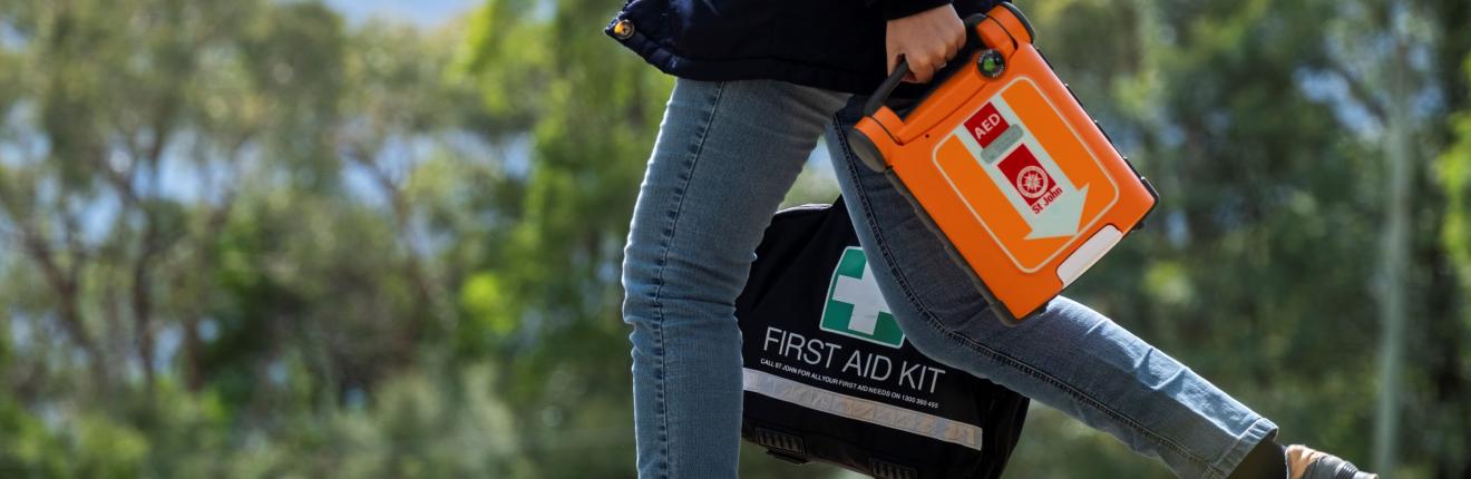 Woman walking in bush holding a St John defib and first aid kit