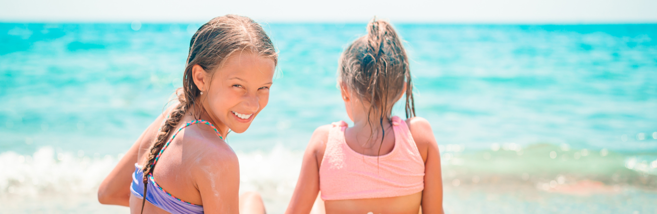 Two young girls apply sunscreen at the beach