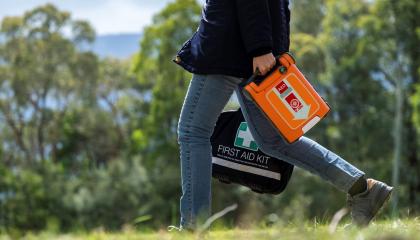 Woman walking in bush holding a St John defib and first aid kit