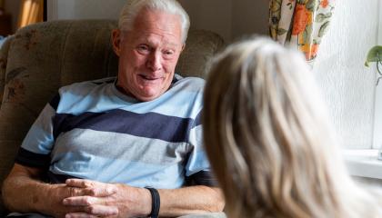 An older man sitting in a chair speaking to a volunteer