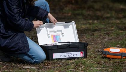 Person kneeling on ground looking inside a first aid kit