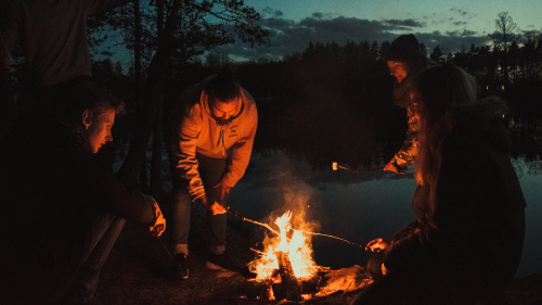  People gathered around a campfire at dusk, roasting marshmallows..