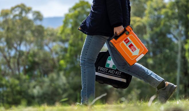 Woman walking in bush holding a St John defib and first aid kit