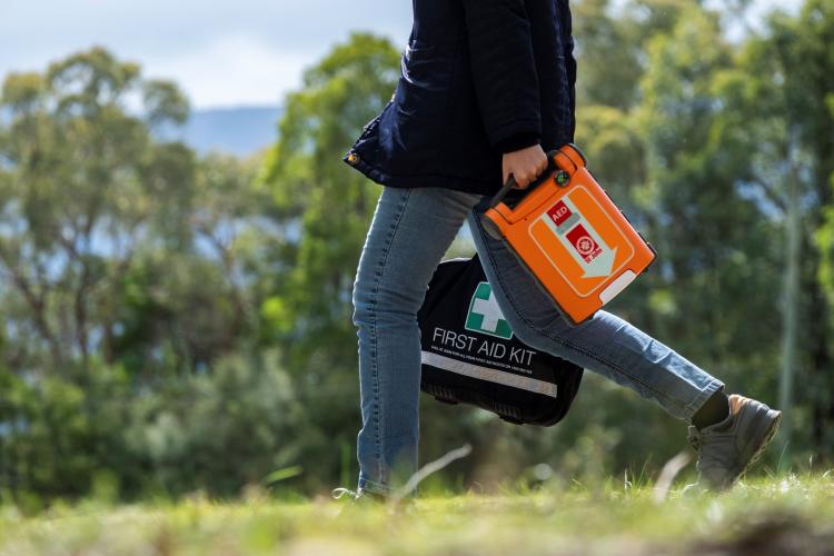 Woman walking in bush holding a St John defib and first aid kit