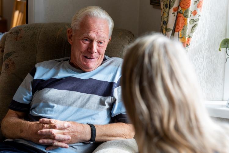 An older man sitting in a chair speaking to a volunteer